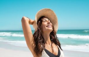 Joyful woman with straw hat enjoying sunny day at a beach.
