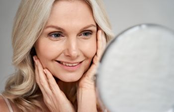 Satified mature woman looking at her face in a mirror.