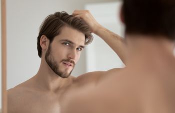 A young concerned man watching his forehead in a mirror.