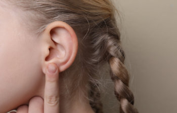 girl pointing at her ear on beige background