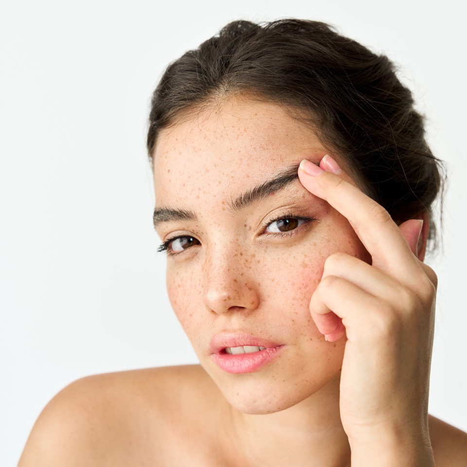 Young adult Latin woman, cool brunette gen z girl with freckles on face looking at camera lifting eyebrow isolated on white background. Beauty aesthetic portrait. Skincare, eye surgery and cosmetic ad
