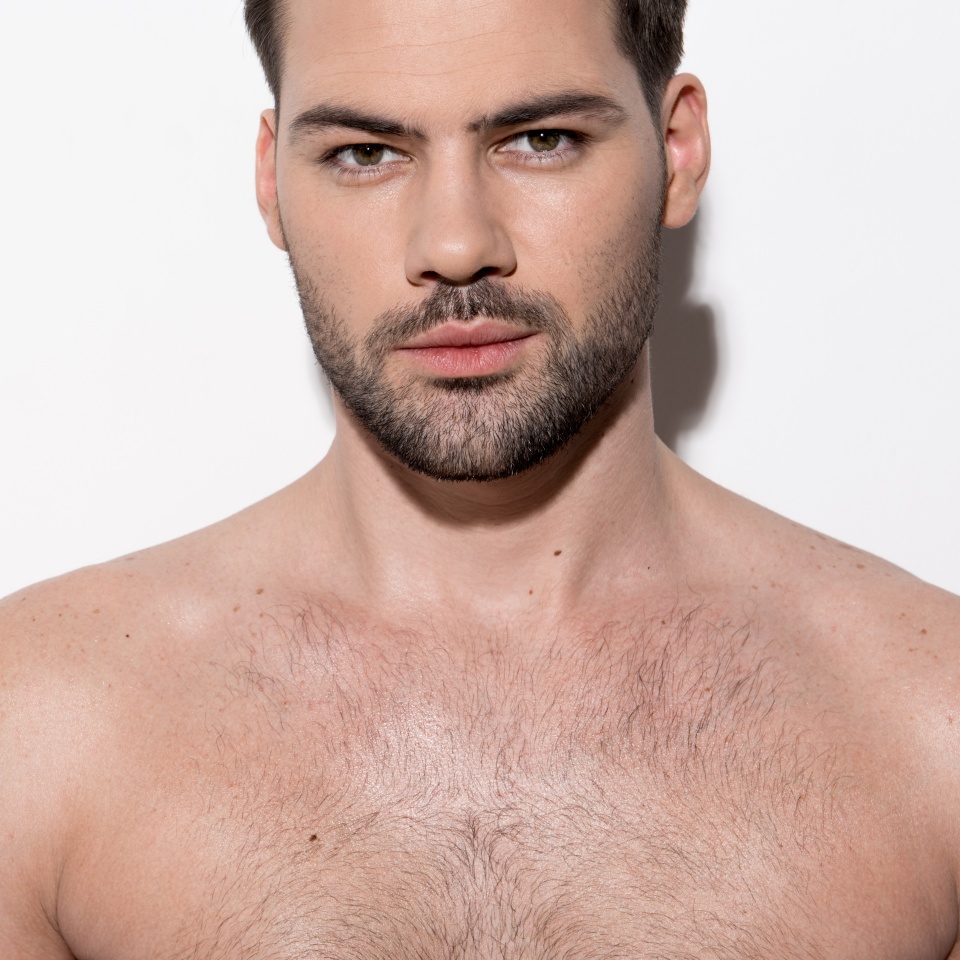 Healthy and beauty concept. Portrait of gorgeous cute bearded guy is standing against light background and looking at camera seductively