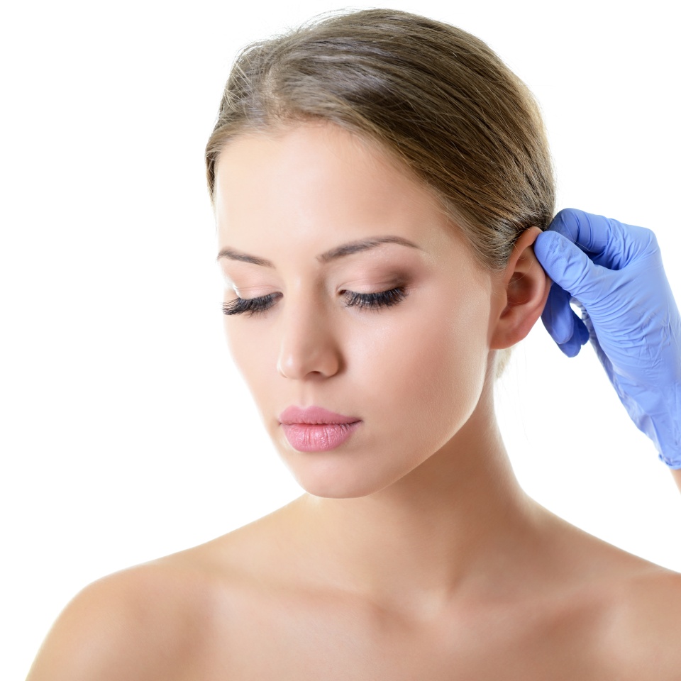 Young beautiful female face, doctor's hand in gloves touchs ear of woman, isolated on white. Beauty treatment, lifting, skincare, plastic surgery concept.