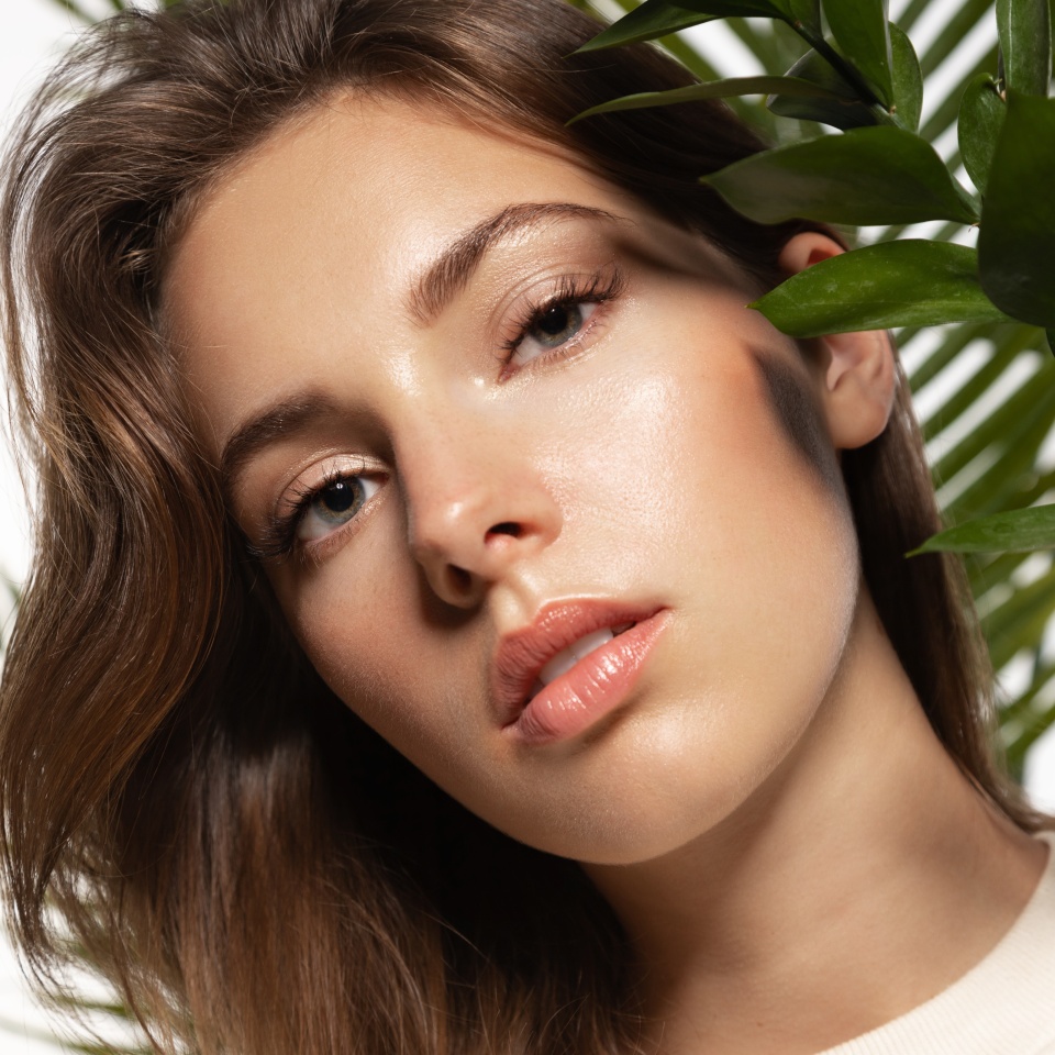 Beautiful woman with perfect skin and natural make-up holding tropical leaves