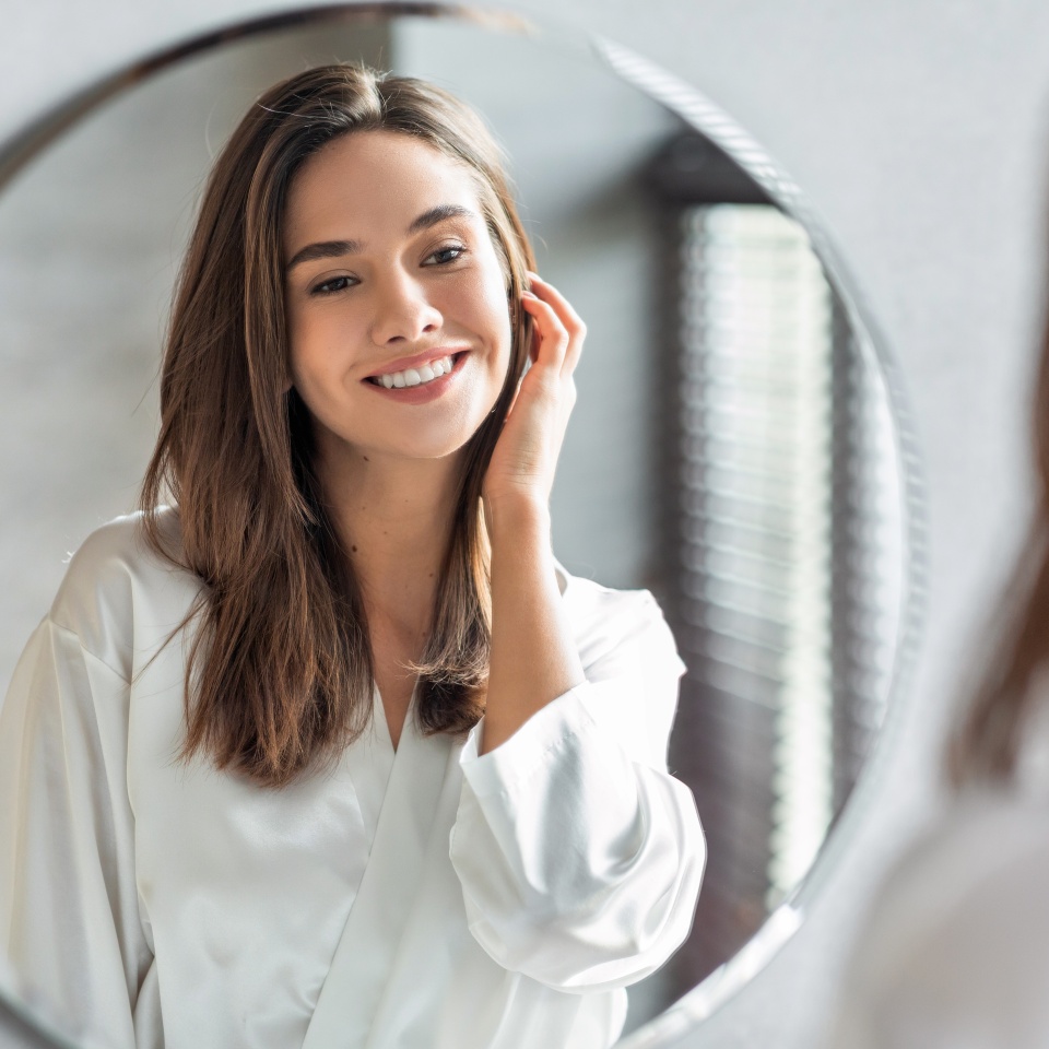 Beauty Concept. Portrait Of Attractive Happy Woman Looking At Mirror In Bathroom, Beautiful Millennial Lady Wearing White Silk Robe Smiling To Reflection, Enjoying Her Appearance, Selective Focus