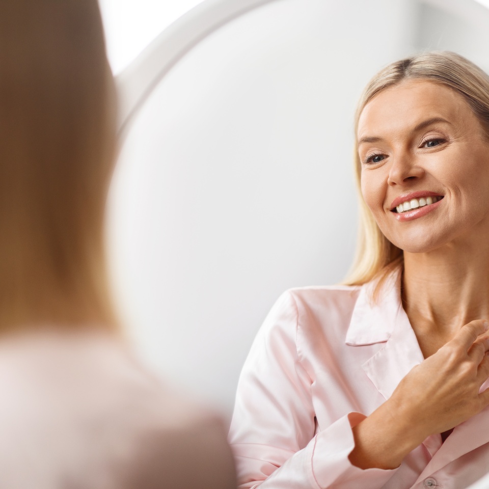 Smiling Attractive Middle Aged Woman Touching Soft Skin On Her Neck While Looking In Mirror, Beautiful Mature Woman Enjoying Result Of Anti-Aging Skincare Treatments, Selective Focus To Reflection