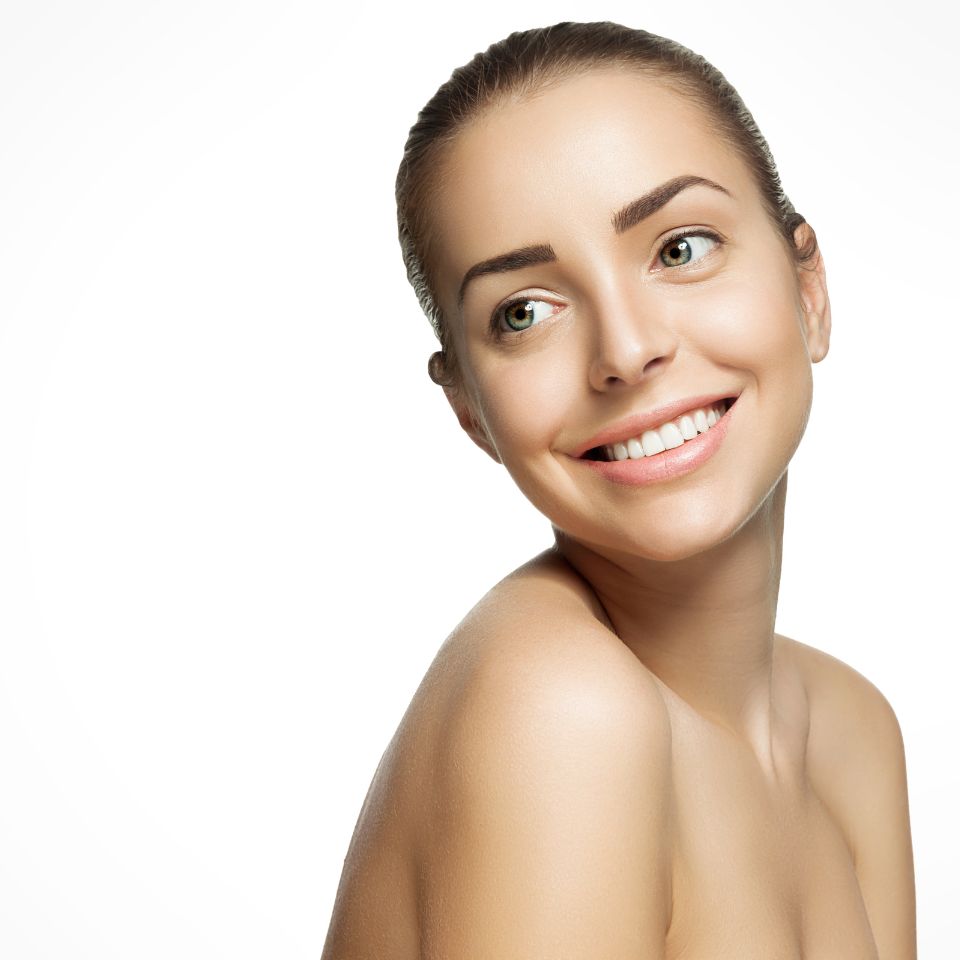 A woman with tied-back hair smiles while looking to the side, against a plain white background.