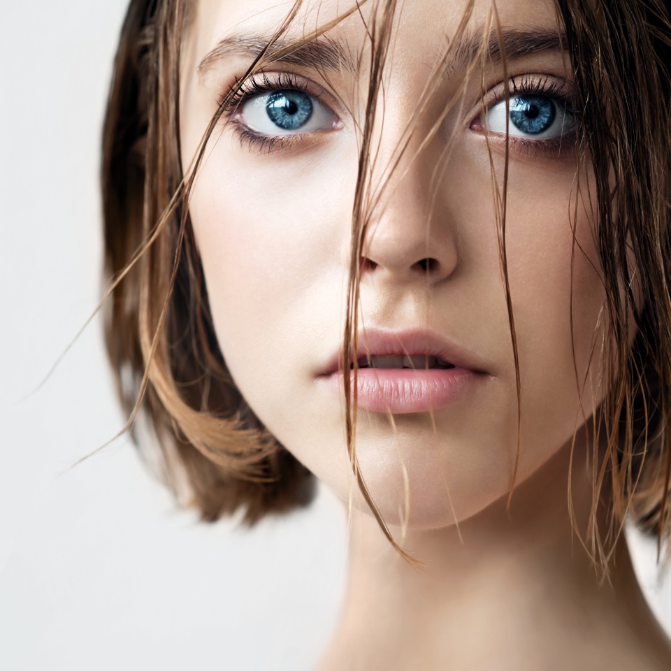 Beautiful young woman with clean perfect skin and wet hair. Portrait of beauty model with natural nude makeup moisturizing her skin. Spa, skincare and wellness. Close up, background, copy space.