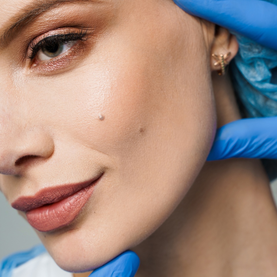 Closeup consultation with plastic surgeon on white background. Cosmetic rejuvenating facial treatment. Doctor man with blue medical gloves touches girl face. Patient ask about lips and chin injections