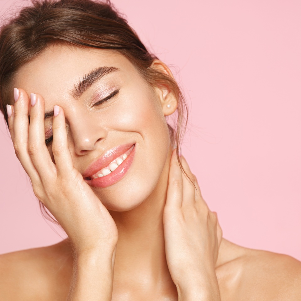Beauty and women concept. Smiling girl with nude makeup and white teeth standing naked on pink background. Young woman touching clean healthy skin, enjoying deep hydration and moisturizing effect.