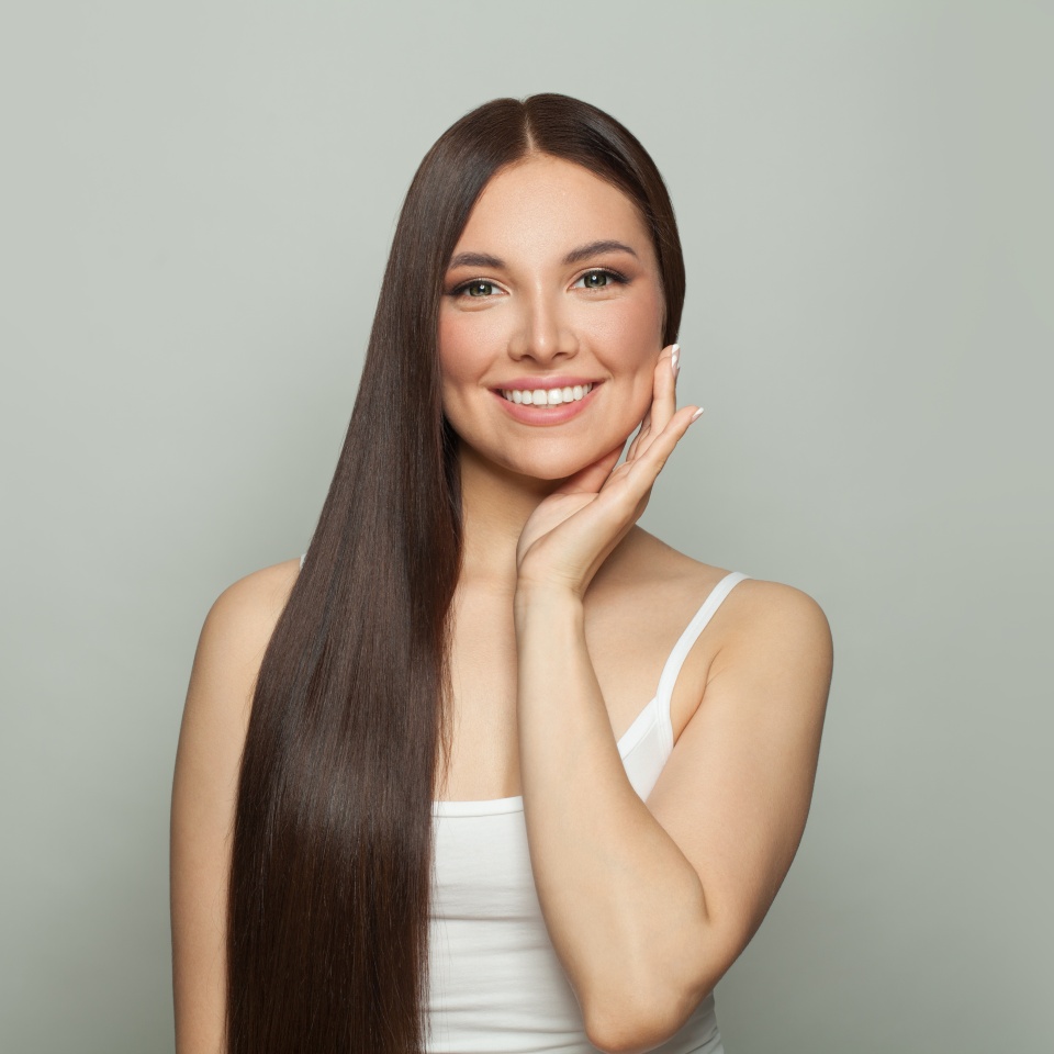 Happy pretty model woman with clear skin and long healthy straight hair smiling on white background. Skincare and facial treatment concept