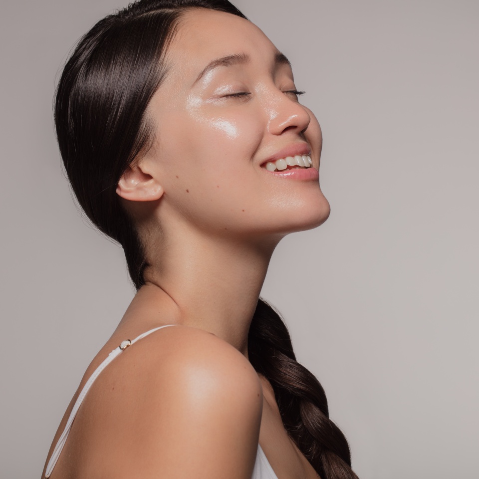 Asian woman with beautiful and healthy skin on beige background. Girl smiling with her eyes closed.