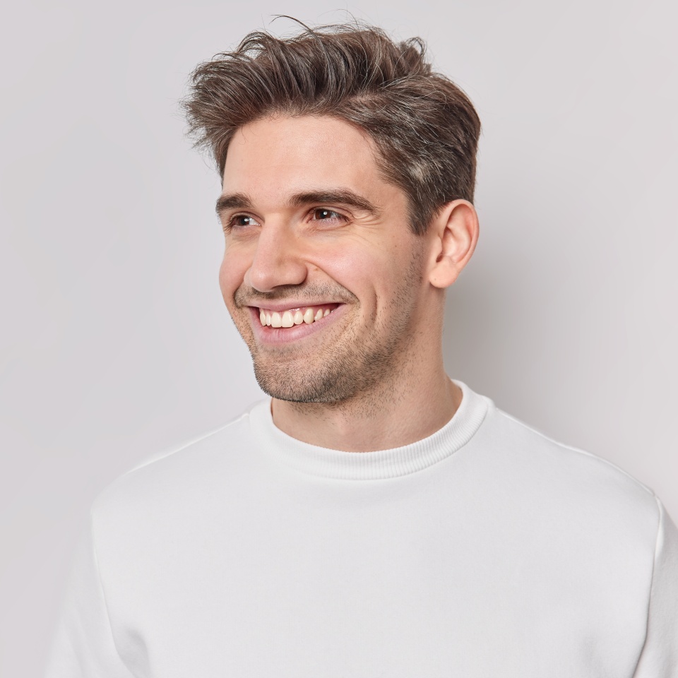 Horizontal shot of handsome pleased European man looks away with happy smile on face dressed casually feels satisfied notices something into distance isolated over white bacground blank copy space