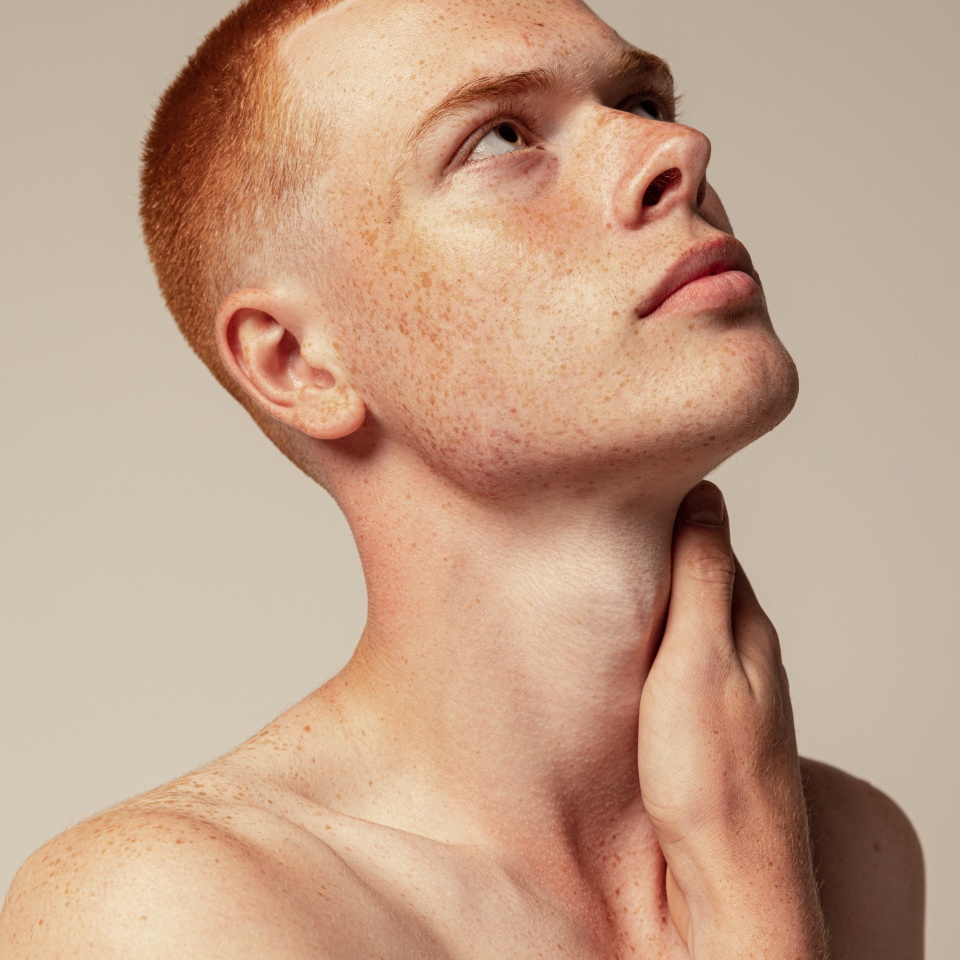 Close-up portrait of handsome young red-haired man posing isolated over grey studio background. Male natural beauty. Concept of men's health, posing, beauty, body and skin care. Thoughtful look