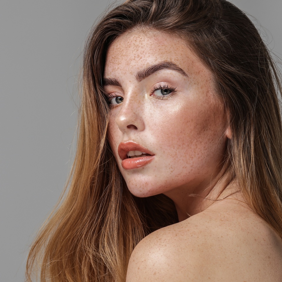 Studio beauty portrait of very natural woman with freckles on her face and shoulder. Girl looking at the camera. A lot of copy space. Skin care concept. Ideal, delicate makeup.