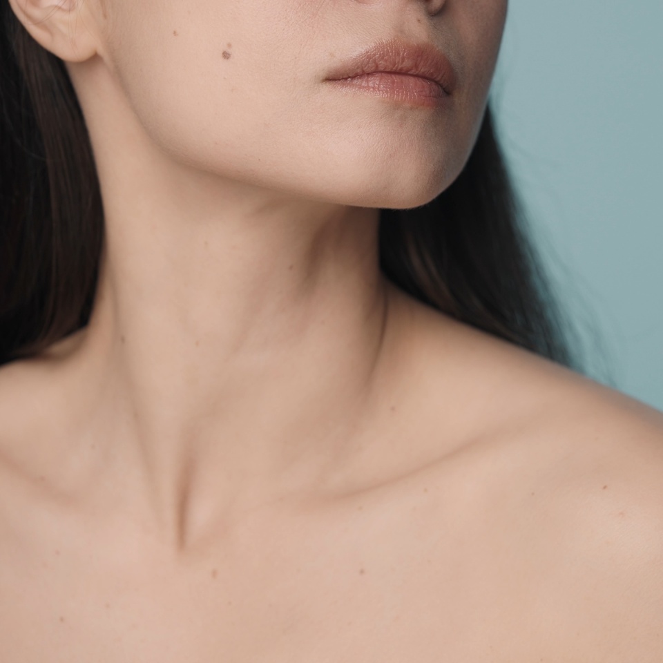 Perfect chin, slender neck and naked shoulders of a woman on a blue background close up. Skin care, body care, cosmetology, plastic surgery