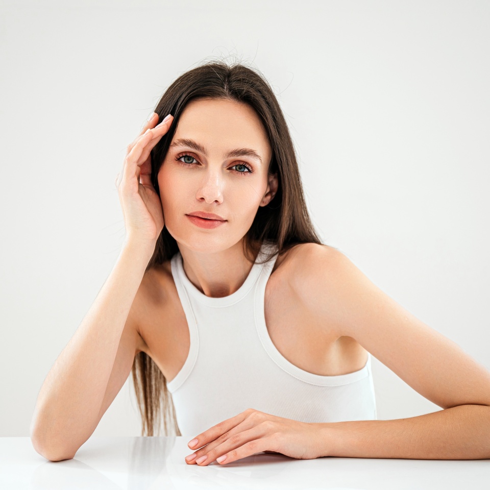 advertising of skincare and bodycare concept. studio shot of young woman with healthy radiant skin looking at camera, hold hand near face, standing isolated against copy paste grey background