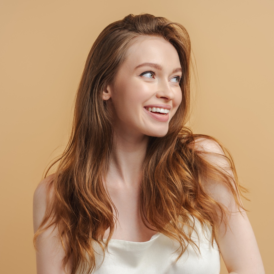 Portrait of beautiful smiling woman with long hair looking away isolated on beige background. Morning routine, healthy lifestyle, hair care concept