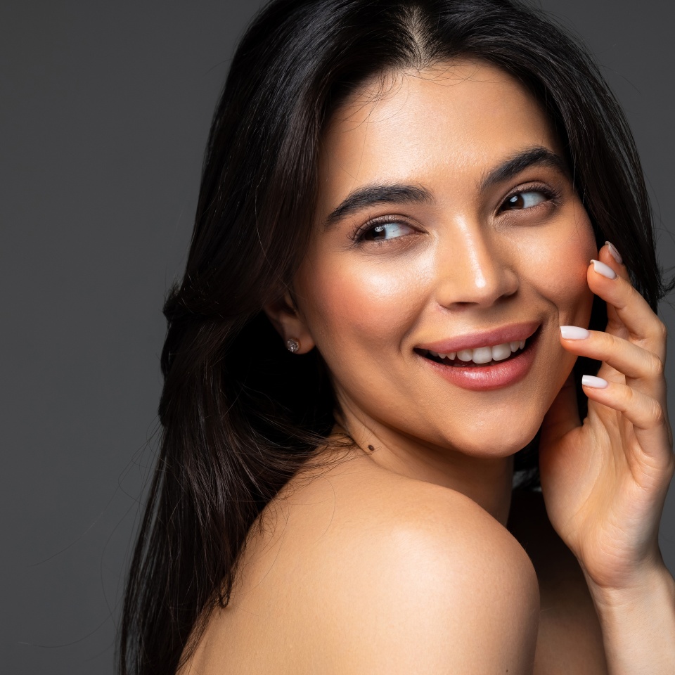 Beautiful young woman with clean perfect skin. Portrait of beauty model with natural nude make up and touching her face. Spa, skincare and wellness. Close up, white background, copyspace