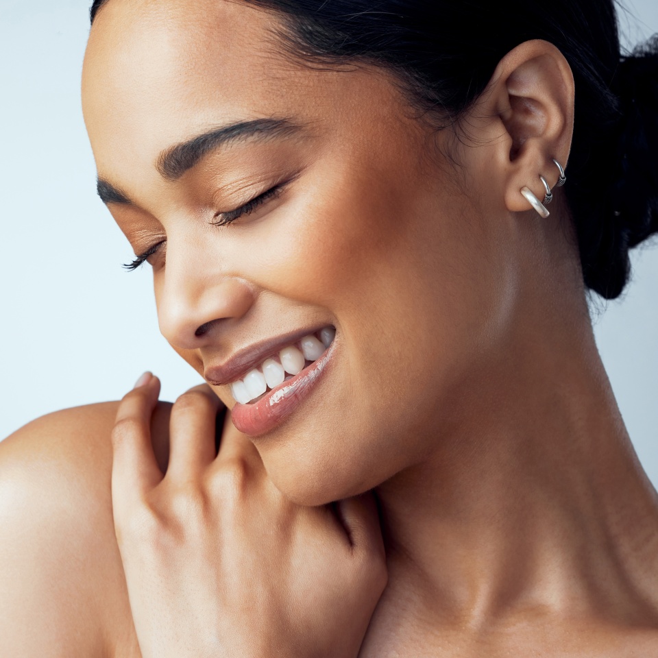 Beauty, skincare and smile with face of woman in studio on gray background for aesthetic or cosmetics. Happy, satisfaction and shoulder with confident model touching skin for dermatology or wellness