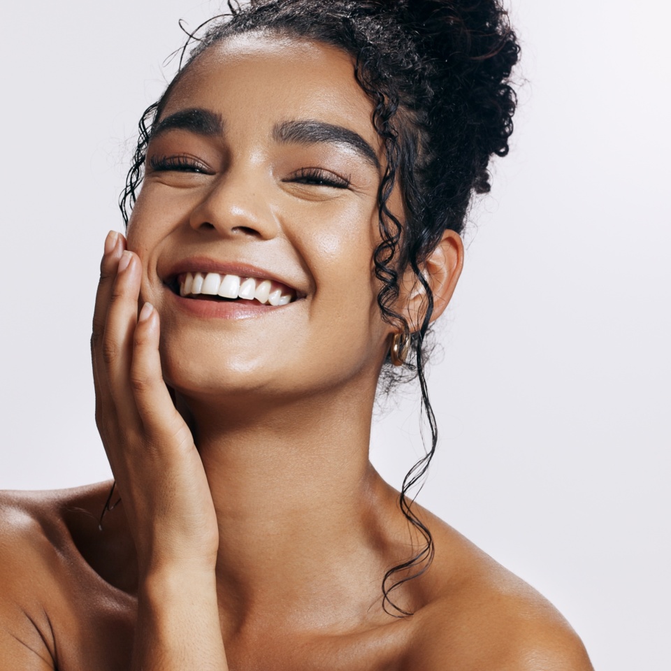 Studio, shine and portrait of woman, touch and treatment of skincare, soft and glow of body in results. Pink background, face and proud for skin, dermatology and cosmetics for person and hand