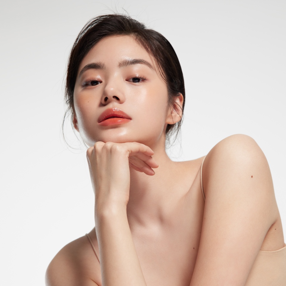 Elegant Portrait of a Woman With Natural Makeup and Glossy Lips, Posing Gracefully Against a Minimalist White Background.