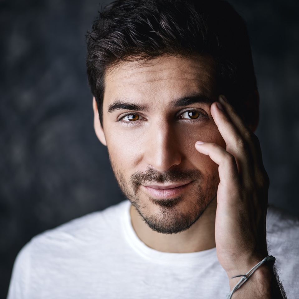 Portrait of a handsome smiling young man wearing white t-shirt. Studio shot over dark background. Men's beauty and health.