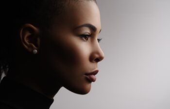 Closeup fashionable portrait of a metis young woman with perfect smooth glowing skin, full lips, collected hair and long neck. Studio photo of an african american female model face, profile