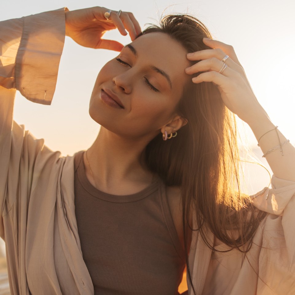 Close-up of young caucasian relaxed woman touching her hair in bright sunlight.