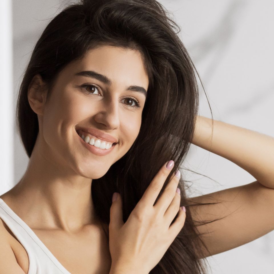 Happy young woman touching her hair and smiling looking in mirror