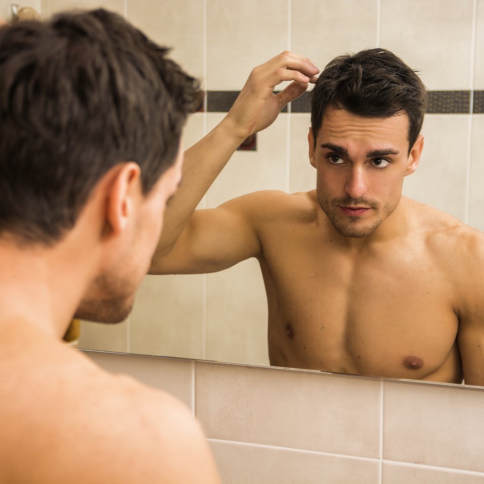 Handsome man looking at his face in mirror, checking hair and hairline