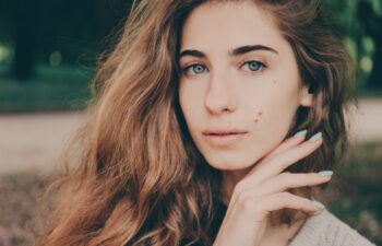 Portrait of a beautiful authentic curly-haired girl in the park in a light beige sweater with blue eyes and birthmarks on her face. No makeup.
