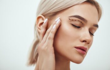 Plastic surgery. Beautiful young blonde woman keeping eyes closed and touching her face with sketch on it