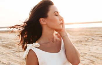 Close up of a beautiful young woman wearing summer dress posing while standing at the sunny beach, eyes closed