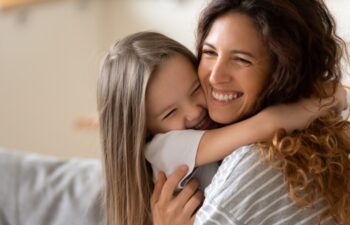 Cute little girl hug cuddle excited young mum show love and affection, smiling mother and funny small preschooler daughter have fun at home embrace sharing close tender moment together