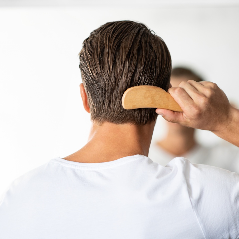 Hair Care. Close up rear view of young man hairbrushing with comb, looking in mirror