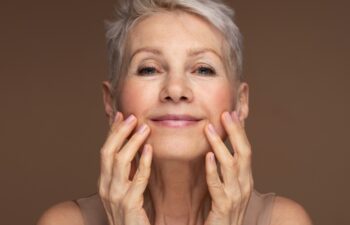 Portrait of gorgeous happy mature woman, senior older 60 year lady looking at camera touching her face