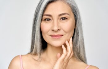Closeup portrait of gorgeous happy middle aged mature asian woman, senior older 50 year lady looking at camera touching her face isolated on white. Ads of lifting anti wrinkle skin care treatment.