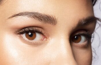 Close up of brown eyes of beautiful woman with modern makeup, shaped perfect trendy eyebrows. Female with smooth healthy skin under eye looking at camera. Make-up and skincare cosmetics advertising.