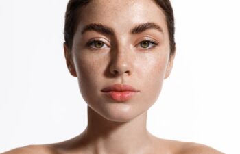 Skin care. Beauty woman with freckles, thick eyebrows and pink lips, has clear perfect skin, face with natural glow after cosmetic cream, spa effect, white background