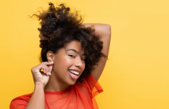 smiling african american woman showing listening gesture while touching earlobe isolated on yellow