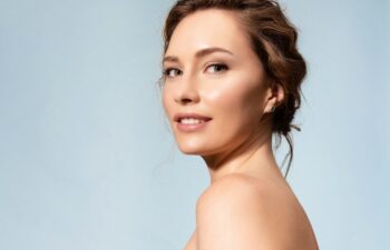 Pretty female with healthy glowing moisturized skin, bare shoulders looking at camera. Studio portrait of woman pleased with skincare antiaging treatment procedure. Natural beauty, organic cosmetics