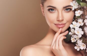 Beautiful young woman with clean fresh skin touching her face in flowers . Girl facial treatment . Cosmetology , beauty and spa . Female model, care concept