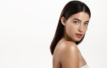 Gorgeous brunette woman with blue eyes, clear glowing skin, perfect shiny body after spa effect, doing nourishing skincare routine, spa at home, standing over white background.