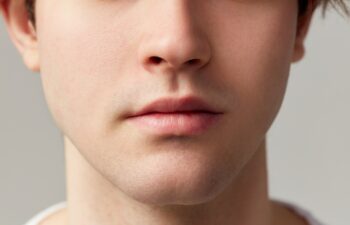 Cropped image of male face nose, lips, chin. Young model posing over grey studio background. Well-kept skin. Concept of men's health, body and skin care, hygiene and male cosmetology