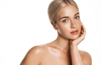 Beauty skin. Head and shoulders of blond woman model, touching glowing, hydrated facial skin, apply toner, skin cream or lotion for healthy look, after shower portrait, white background.