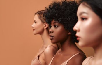 Multi-ethnic multiracial young women in beige lingerie isolated on a beige background. African-American, Caucasian and Asian women posing in the studio. Concept of face body skin care, cosmetology.