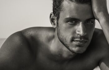 Sexy closeup portrait of handsome topless male model with beautiful eyes on the beach. Black and White.