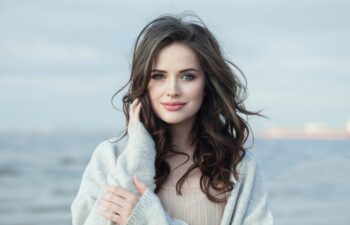 Young female model with makeup, clean skin, healthy hairstyle and friendly smile on sea beach. Natural beauty woman portrait
