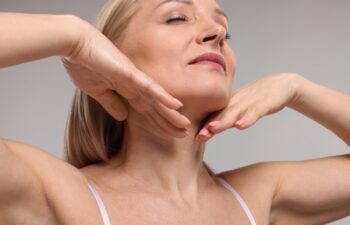 Beautiful woman touching her neck on grey background, closeup